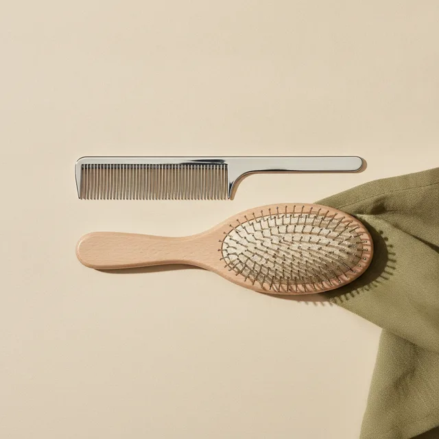 A steel grooming comb and an oval pin brush on cream paper