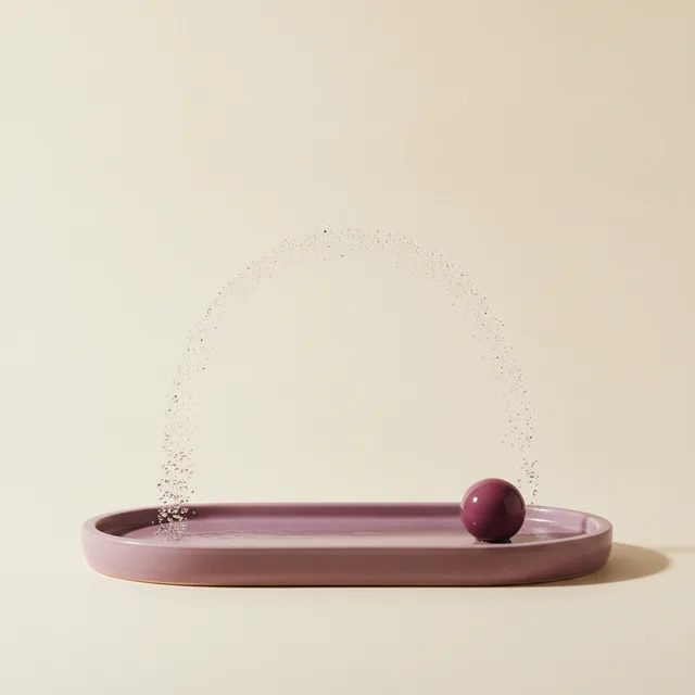 A fine arc of atomised mist above a plum ceramic tray