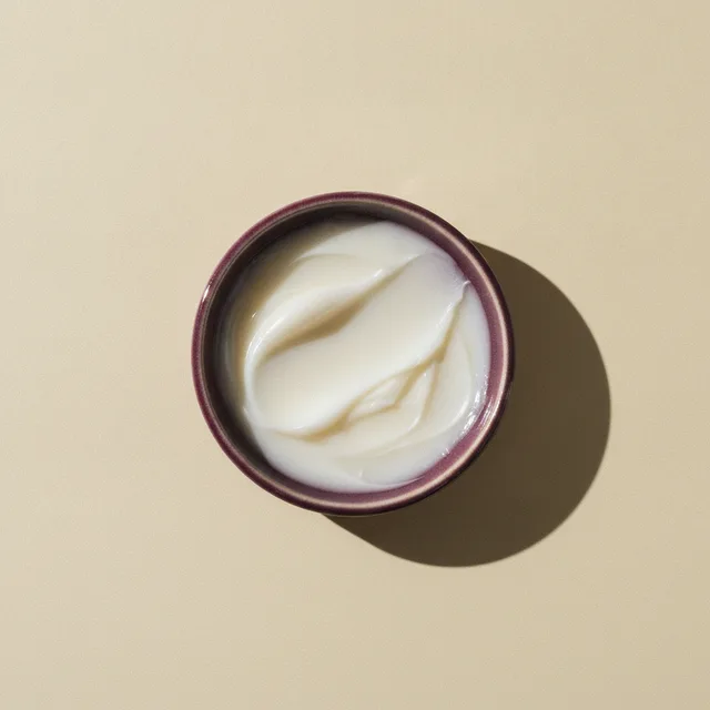 A swirl of pearl-white conditioning balm in a deep plum dish
